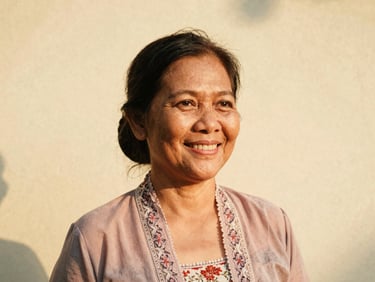 Candid portrait of a smiling Indonesian woman in her 50s, warm natural golden-hour light, slightly faded analog tones, 35mm film aesthetic, wearing a traditional kebaya, looking approachable.