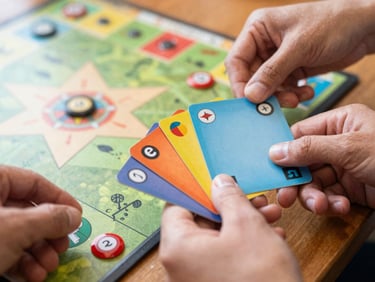 A close-up of hands holding colorful resource cards over a wooden board game, warm lighting, shallow depth of field