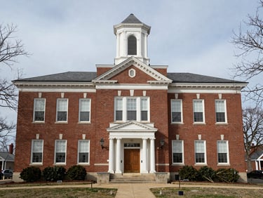 Wide shot of a dense brick county courthouse exterior in a small Ohio town, midday overcast light, bare trees visible at the frame edge, photographed straight-on as documentary record