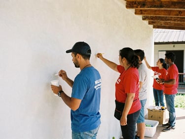 Volunteers of different ages working together to paint a clean white wall of a neighborhood center, bright daylight