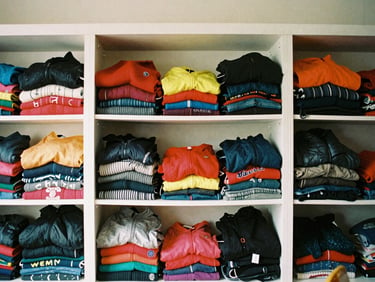 Neatly organized shelves of donated winter clothing, colorful sweaters and jackets, warm indoor lighting