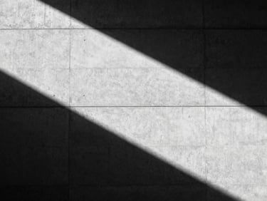 Expansive wide shot of a brutalist concrete building facade, sharp diagonal shadows, hard directional sunlight, minimalist composition, black and white