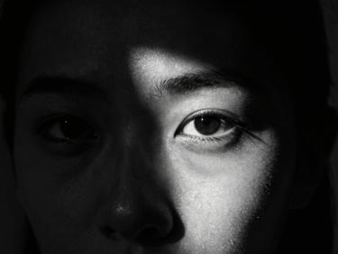 A dramatic chiaroscuro portrait of an artist, half-face in deep shadow, sharp focus on the eye, high-contrast black and white
