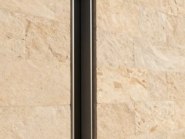 Close-up of local stone wall meeting a minimalist steel window frame, warm afternoon sun, high-end architectural craft