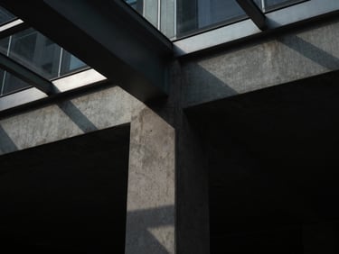 Clean architectural detail of a concrete column meeting a glass ceiling, sharp geometric shadows, dramatic low-key directional light, 35mm lens.
