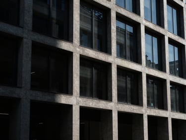 Wide architectural perspective of a concrete and glass building facade, dramatic directional light, cool shadows, dark editorial style