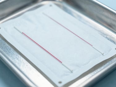 Macro shot of sterile surgical suture packaging on a stainless steel clinical tray, bright cool-toned lighting.