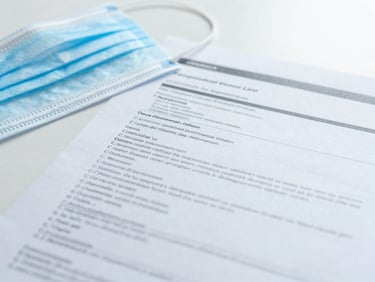 Close-up of technical medical compliance documents on a white desk beside a sterile surgical mask.