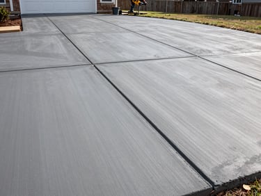 Freshly poured and finished concrete driveway at a Columbus Georgia home, smooth gray surface with crisp expansion joints, crew troweling the far section, natural daylight, wide environmental framing