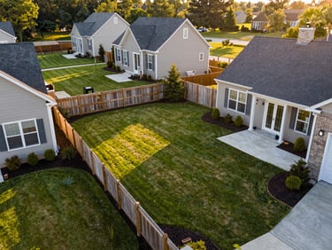 Aerial-angle wide shot of a Columbus Georgia residential backyard showing multiple completed improvements — manicured lawn, raised mulch bed, wooden fence line, concrete patio pad — golden hour light across the whole property