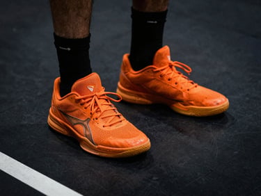 Gritty athletic photography, low-angle tight crop on a player's squeaking orange sneakers on a dark charcoal court, high-contrast lighting.