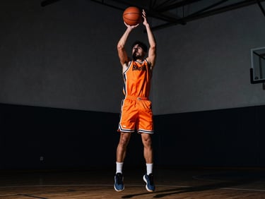 Action shot of a basketball player executing a perimeter pull-up jumper, high-contrast dramatic indoor court lighting, deep shadows.