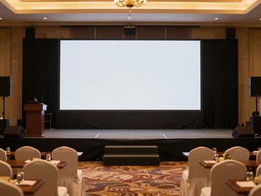Medium shot of a well-organized corporate event stage with a clear presentation screen and elegant seating arrangements in a local Mysuru venue, ambient event lighting.