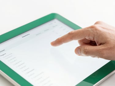 Close-up of a hand tapping a clean tablet screen showing technical inventory data, bright high-key white daylight, emerald green accents, sharp focus