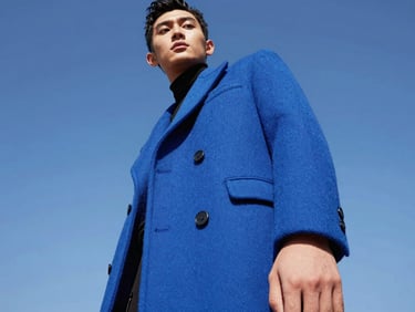Model in low-angle heroic pose wearing an electric blue tailored coat, direct bright sunlight