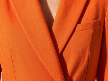 Close-up of vibrant orange structured fabric with sharp tailoring details, high-contrast studio lighting