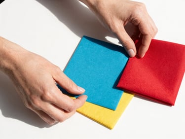 Close-up of hands arranging bold accessories and structured fabric swatches on a clean white surface