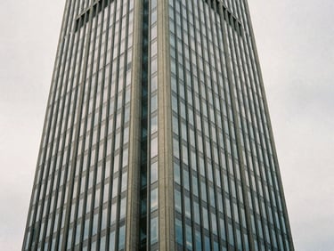 Architectural detail of a minimalist glass skyscraper in Zurich, shot from a low angle against a soft overcast sky, desaturated navy tones, 35mm film grain.