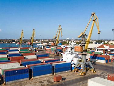 Vue aérienne grand angle du port de Libreville au Gabon, porte-conteneurs bleu à quai sous une lumière naturelle éclatante, grues de déchargement massives.