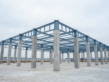 Wide-angle view of a modern industrial warehouse frame under construction, concrete pillars and steel roof trusses, overcast daylight.