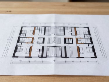 Macro detail of technical architectural blueprints laid out on a clean wooden table, soft natural side light, sharp focus on structural lines