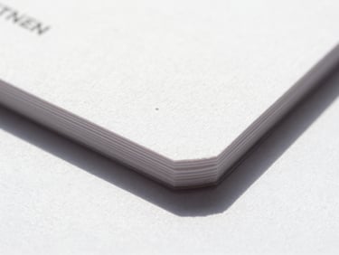 Macro detail shot of freshly printed thick cotton business cards with deep ink saturation, crisp edges, natural daylight casting soft shadows, showing tactile paper texture.