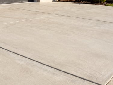 Crisp architectural photo of a newly poured, smooth concrete driveway with clean edges, bathed in bright southern daylight, high-end residential, 35mm lens