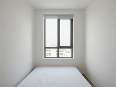 Full-room shot of a compact Dubai apartment bedroom, clean white walls, minimal furniture, even window daylight revealing proportion and finish quality, no people