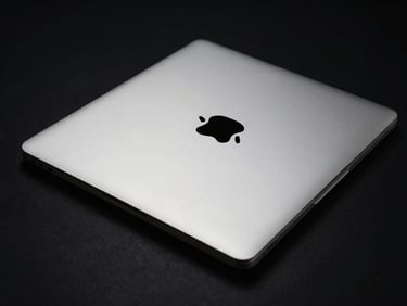 Angled studio shot of a silver MacBook Air M1, closed, showing its ultra-thin wedge profile, metallic reflections, low-key dramatic lighting, black background