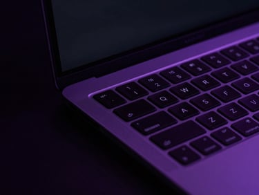 Overhead macro shot of a sleek laptop showing a dark clean user interface with vibrant purple neon accents, high contrast studio lighting