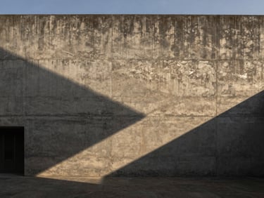 Wide-angle architectural photography of a raw concrete facade in Medellín, dramatic golden-hour light casting long geometric shadows, high-contrast, minimalist design.