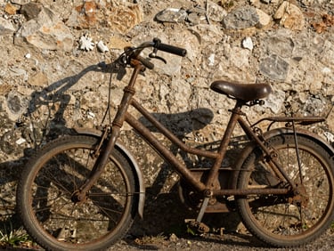 Détail d'un vieux vélo d'enfant rouillé appuyé contre un mur de pierre ensoleillé