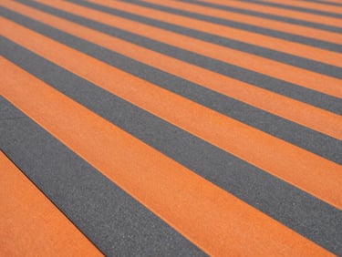 Macro texture shot of orange and charcoal interlocking PP sports tiles, clean architectural lines, high-contrast industrial tones