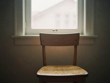 Soft sunlight filtering through a window onto an empty wooden chair, negative space, 35mm film