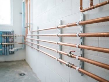 Parallel copper pipes routed neatly along a white utility wall, perfectly straight clips and clean solder joints