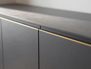 Close-up architectural shot of seamless cabinet joinery, dark matte charcoal finish meeting a delicate gold accent inlay, sharp focus, natural side lighting