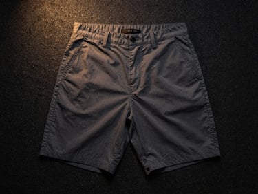 Flat-lay of tailored dark grey casual shorts on a black textured surface, soft golden highlight
