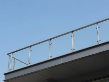 Minimalist balcony with glass guardrails and slim dark aluminum profiles, overlooking a clean blue sky, sharp daylight, low-angle shot.