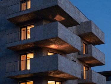 Modern residential building exterior, geometric concrete balconies, warm copper interior lights visible through windows, dusk