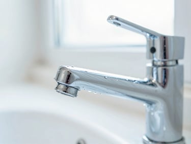 Macro detail shot of a sparkling clean chrome kitchen tap with bright sunlit background, water droplets, shallow depth of field, crisp whites and soft blues.