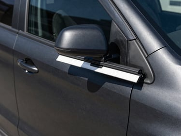 Close-up of a matte black corporate vehicle wrap being applied with a squeegee tool, sharp daylight, high-contrast detail
