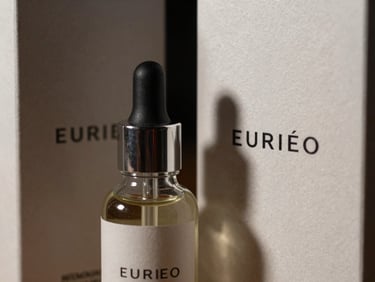 Macro close-up of luxury cosmetic glass bottles with minimalist typography, soft dramatic studio shadows, embossed paper box packaging beside it.