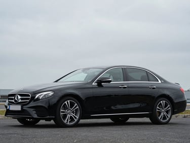 Front three-quarter driver-side profile of a black Mercedes-Benz E-Class, overcast daylight, full vehicle visible, squared frame, no tilt