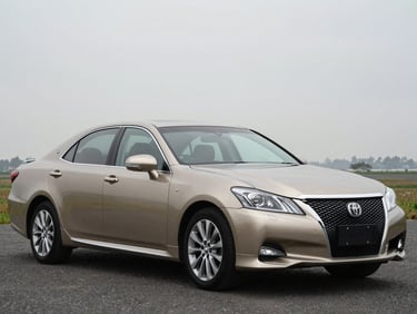 Front three-quarter driver-side profile of a champagne gold Toyota Crown, overcast daylight, full vehicle visible, squared frame
