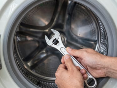 Close-up of hands using a professional wrench on a washing machine drum assembly, focused work light.