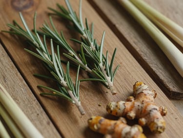 Close-up overhead of dried organic herbs — rosemary, turmeric root, and lemongrass arranged on aged wooden boards under warm overcast daylight, earthy tones and fine texture detail