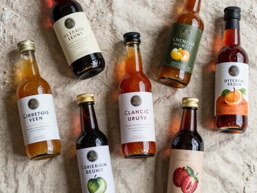 Overhead flat-lay of glass condiment bottles filled with organic sauces and vinegars on a cream linen surface, natural morning light, sharp focus on label texture and liquid color