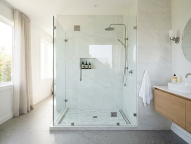 Straight-on architectural photography of a minimalist frameless glass shower enclosure in a bright, modern bathroom, natural daylight, crisp reflections, neutral tones, 35mm lens