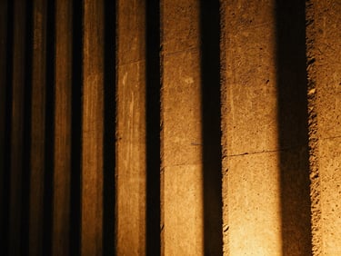 Close-up of warm amber architectural light grazing a rough, textured concrete facade at night, dramatic high-contrast shadows, grainy film texture