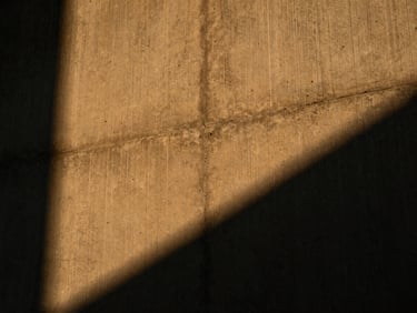Low-angle shot of a textured concrete wall grazed by warm amber light, casting deep dramatic shadows in the crevices.